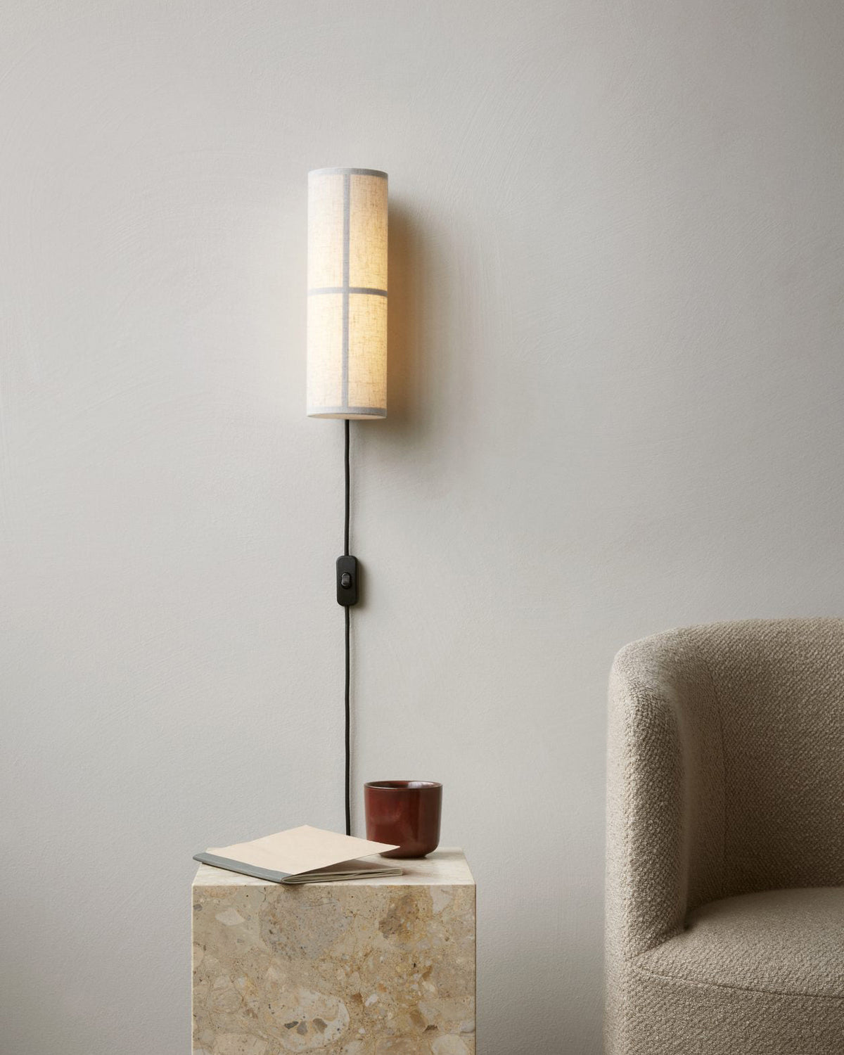 Linocanne Fabric Cylinder Plug-In Wall Lamp, linen lamp lit over travertine side table and boucle chair