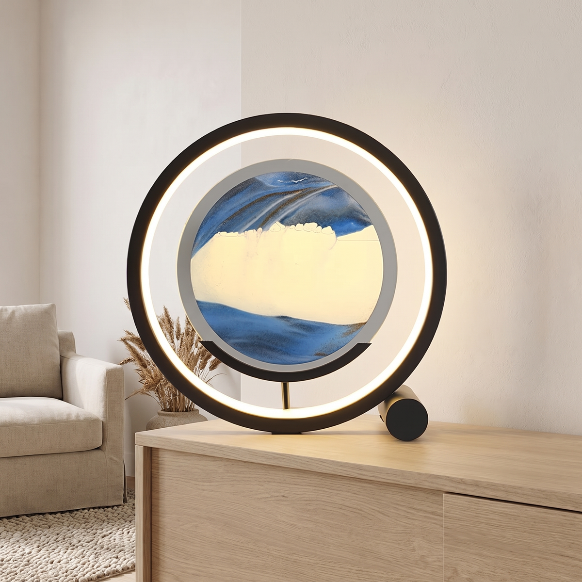 Sandrelle Table Lamp in black with lit LED ring and round blue and cream sand panel, standing on a pale oak sideboard in a living room