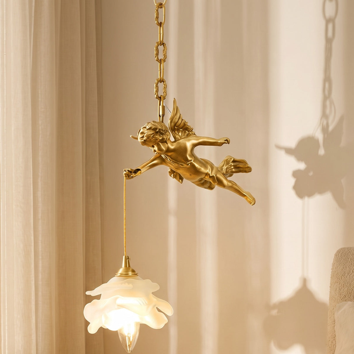 Seraphel Pendant Light in brass with cherub and frosted flower shade, lit, beside sheer curtains in a warm bedroom