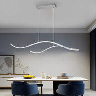 Linear pendant light made of wavy LED bars hung from a slim rectangular canopy, lit, above a dining table with blue chairs.