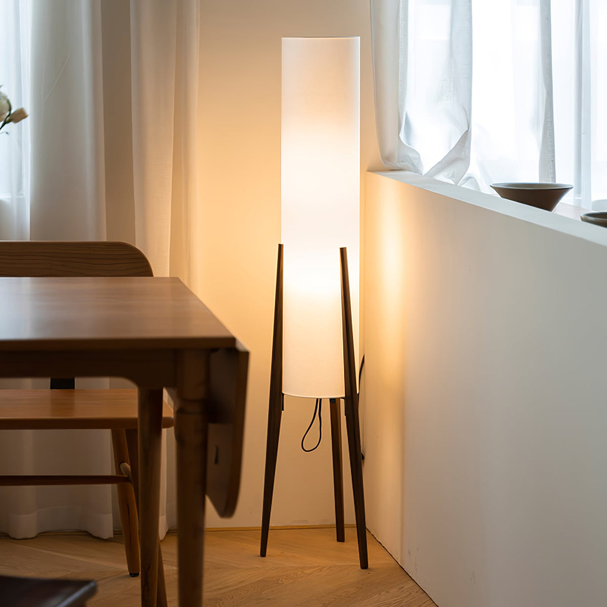 Tavora Walnut Floor Lamp lit in a corner beside a dining table and window