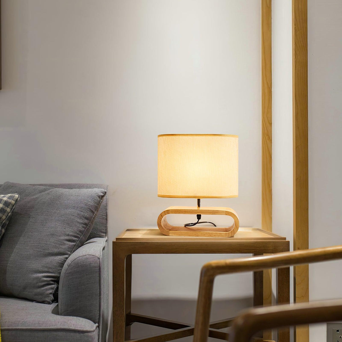 Tavren Wood Table Lamp, lit, on a wood side table beside a grey sofa in a living room