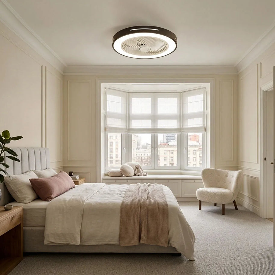 Ceiling fan with a black rim and integrated LED light, fitted flush to a bedroom ceiling near a bay window.
