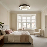 Ceiling fan with a black rim and integrated LED light, fitted flush to a bedroom ceiling near a bay window.