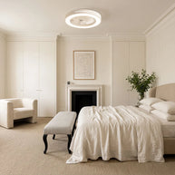 Ceiling fan with a white rim and integrated LED light, fitted flush to a bedroom ceiling above a bed and fireplace.