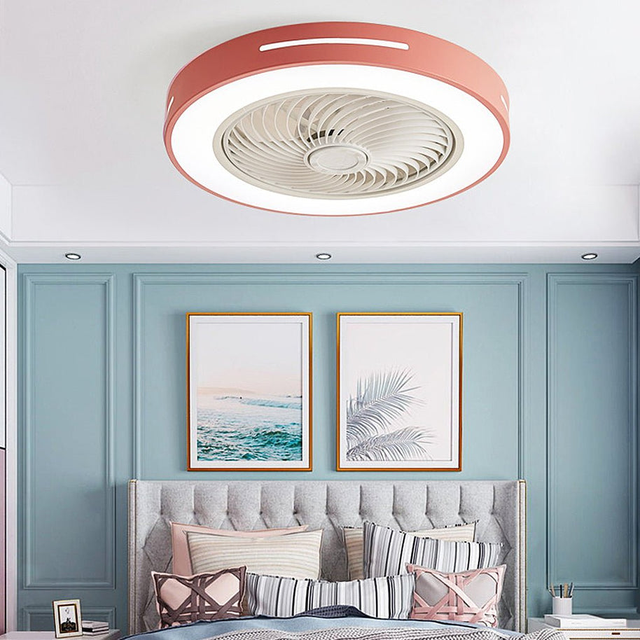 Flush-mount ceiling fan with an enclosed blade cage and a lit ring, pink outer rim, fitted to a bedroom ceiling above a bed with framed prints behind.